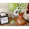 This is an entryway display on an old whiskey barrel. A clock sits next to a green glass candle holder and a handmade gourd vase. 